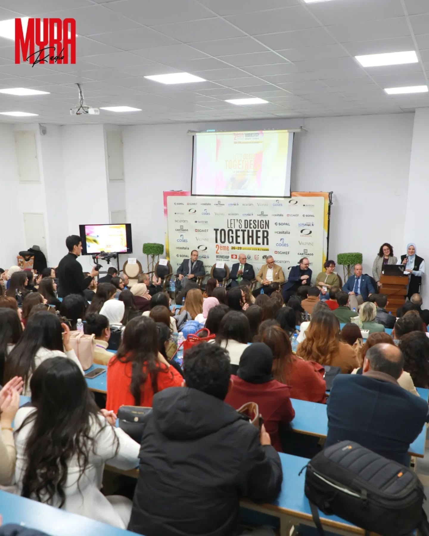 A full lecture hall attending the second Let’s Design Together workshop in Tunisia, with speakers seated in front of the event backdrop.